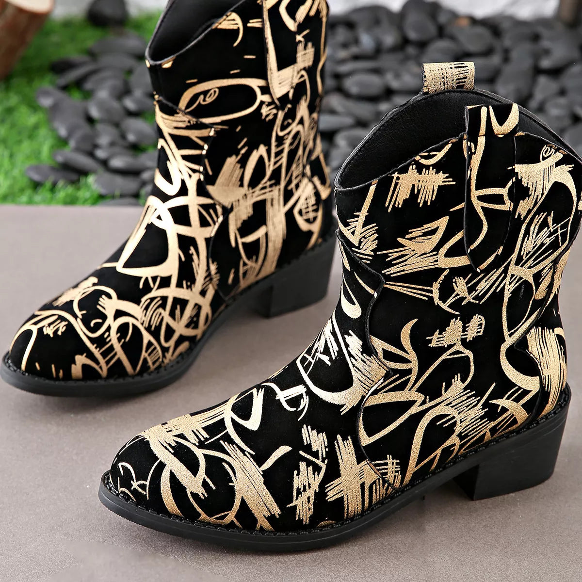 Black and gold patterned boots on a neutral surface with a blurred natural background