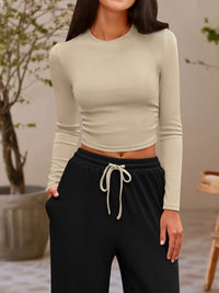 Person wearing a beige long-sleeve crop top and black drawstring pants in an indoor setting.
