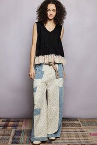 Woman wearing a black sleeveless top and patchwork pants with a belt, standing against a plain background.