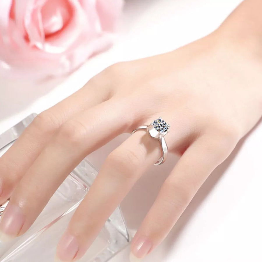 Silver ring with a diamond on a hand against a soft pink floral background