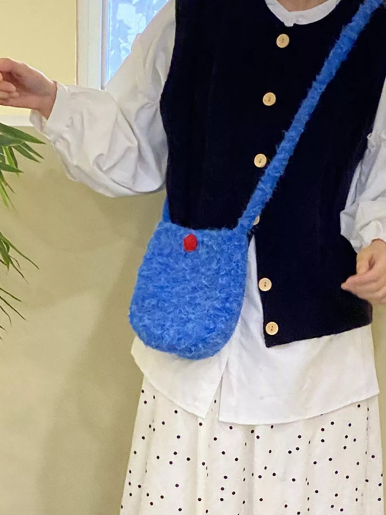 Person wearing a blue textured handbag with a red button, standing indoors.