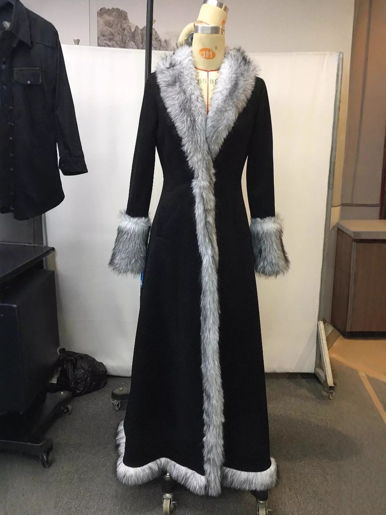 Long black coat with fur trim on a mannequin against a plain background