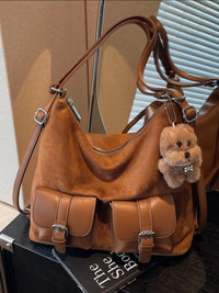 Brown leather handbag with a teddy bear charm on a black surface.