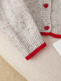 Close-up of a knitted garment with red trim on a beige surface