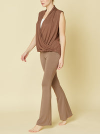 Woman wearing a brown sleeveless top and flared pants on a beige background
