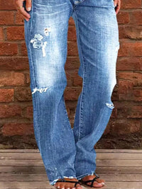 Blue jeans with distressing details worn by a person against a brick wall.