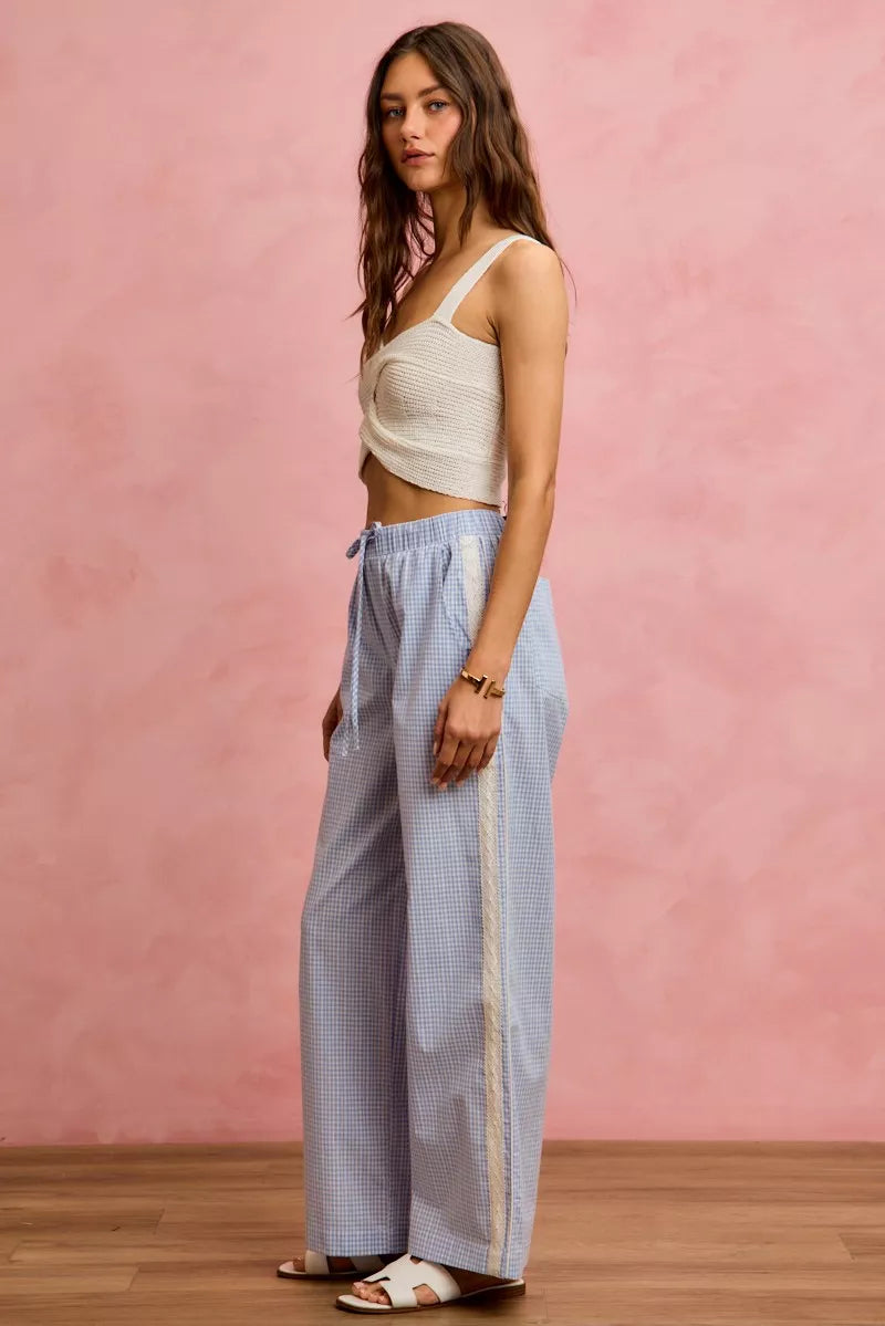 Woman wearing a white top and light blue checkered pants against a pink wall.