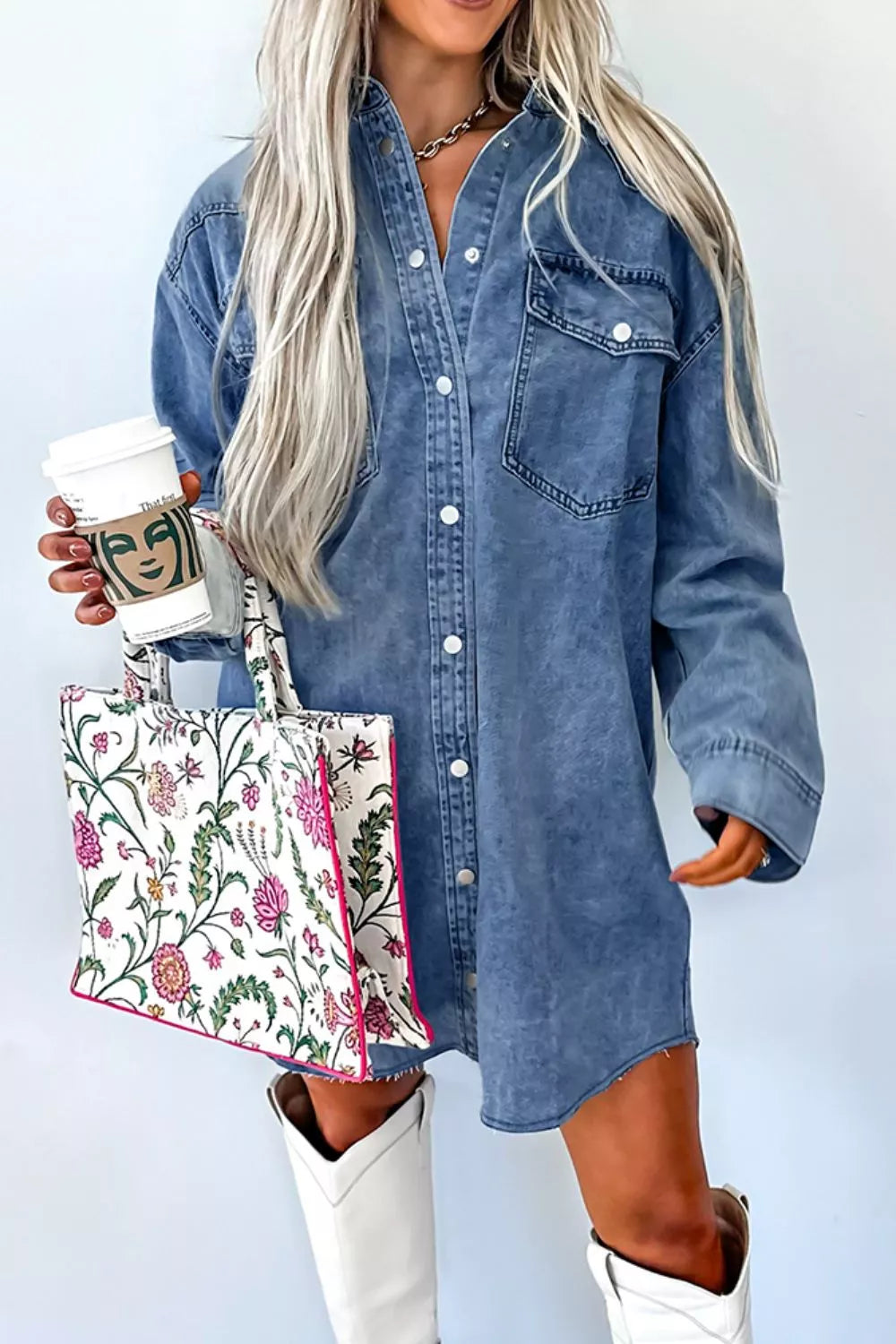 Person wearing a denim shirt dress holding a floral tote bag and a coffee cup.