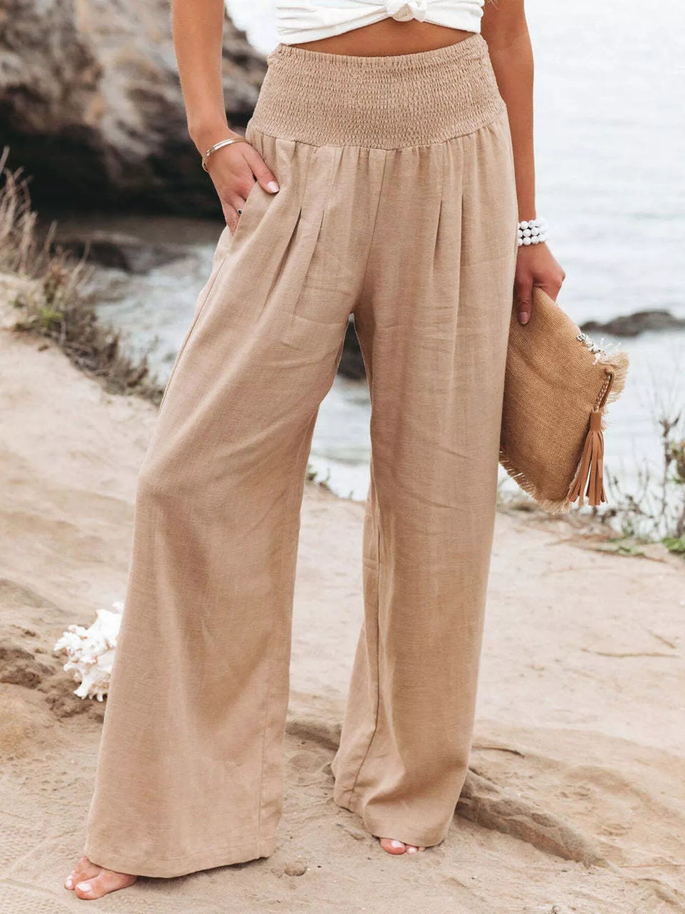 Person wearing beige wide-leg pants standing on a rocky beach with 'NatureQueens' branding.