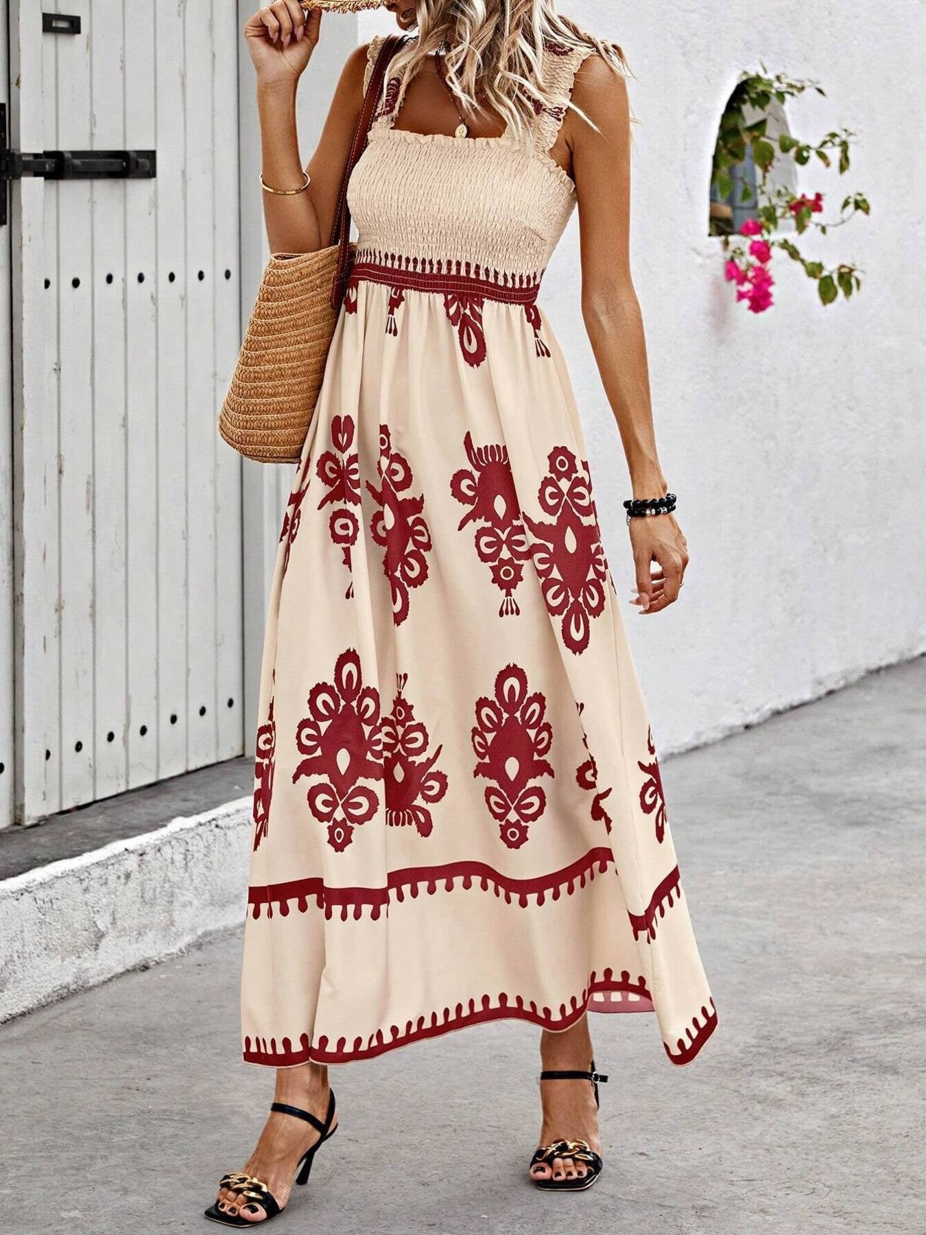Woman wearing a beige dress with red patterns, standing against a white wall.