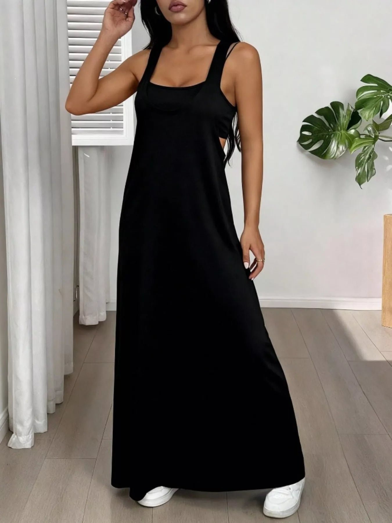 Woman wearing a black dress in a room with white curtains and a plant.