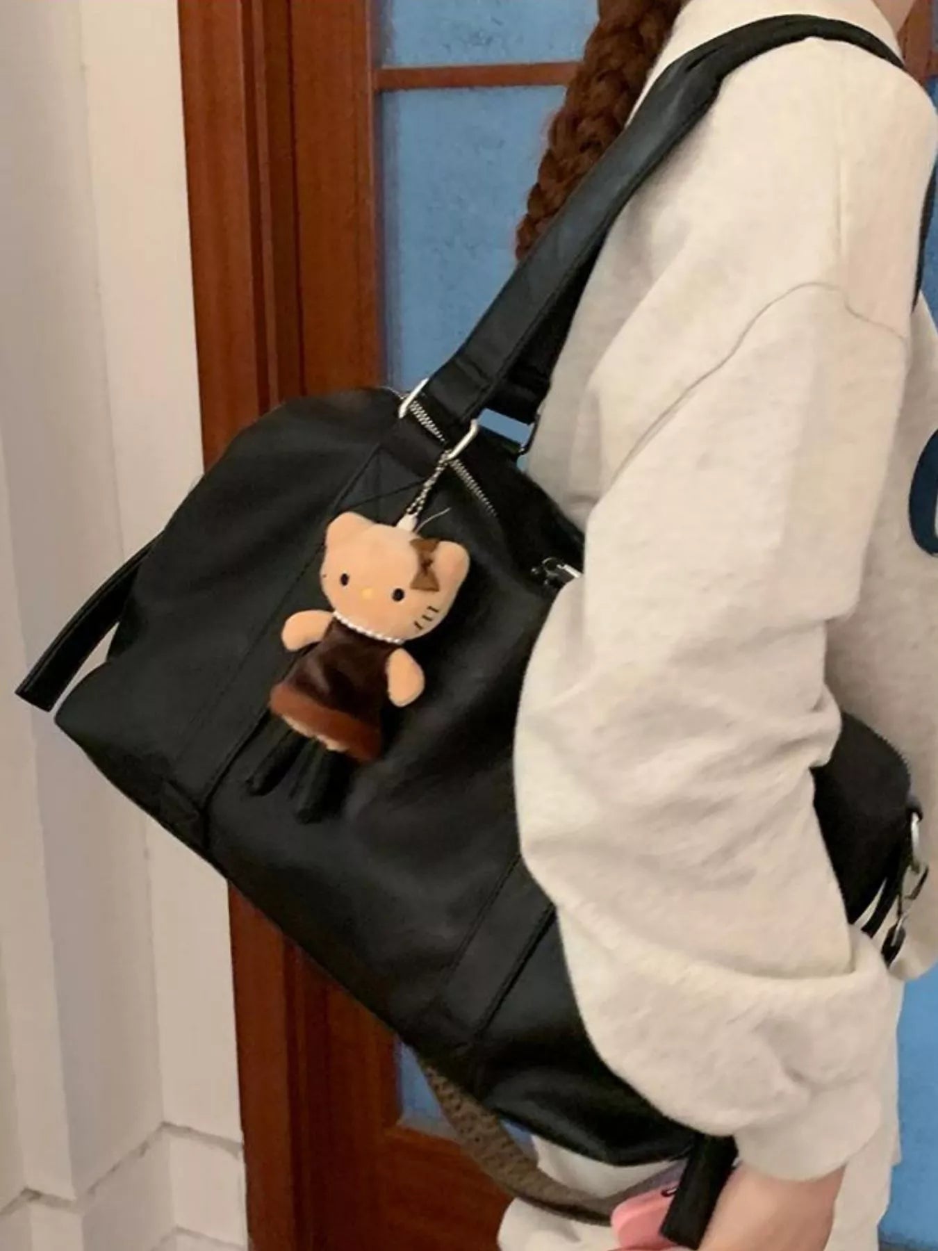 Black bag with a cat-shaped charm held by a person wearing a white jacket.