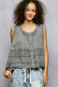 Woman wearing a sleeveless, layered top with a gray and white pattern against a plain background