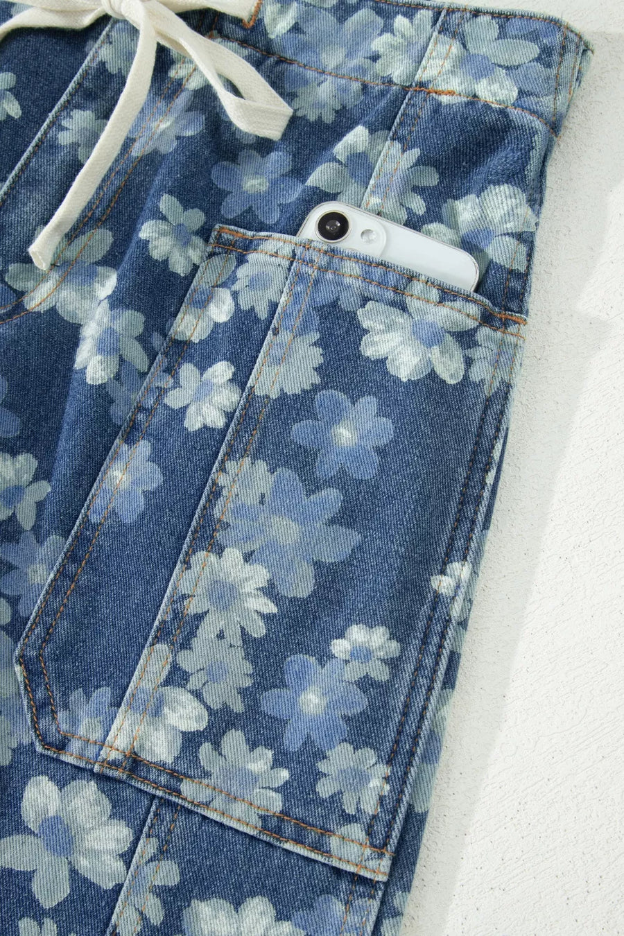 Blue floral-patterned jeans with a white drawstring on a light gray background