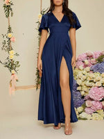 Woman wearing a navy blue dress with a slit in front, standing against a floral background.