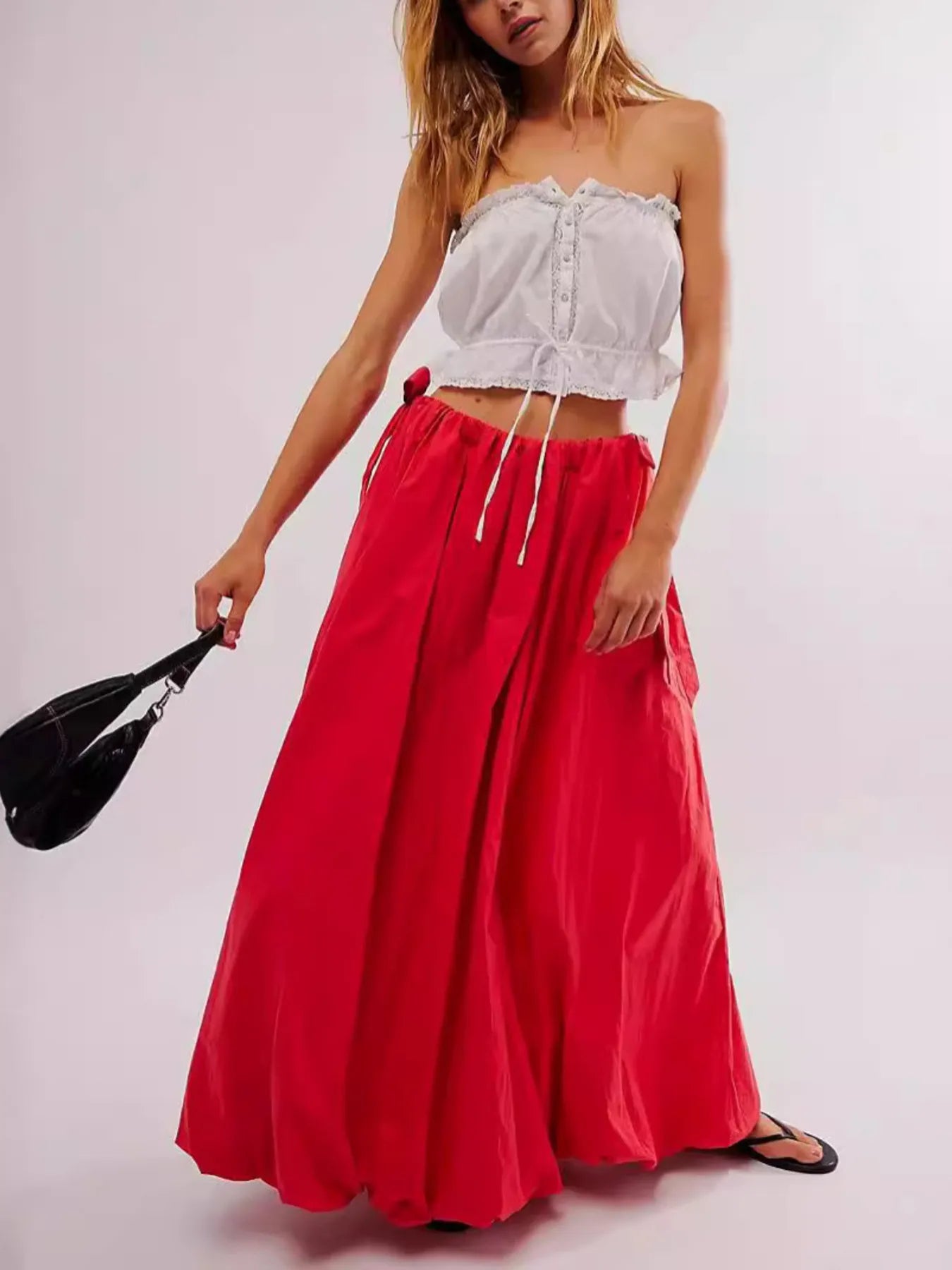 Woman wearing a white strapless top and red skirt against a plain background