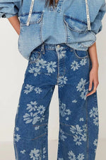 Person wearing a denim jacket and floral-patterned jeans on a plain background