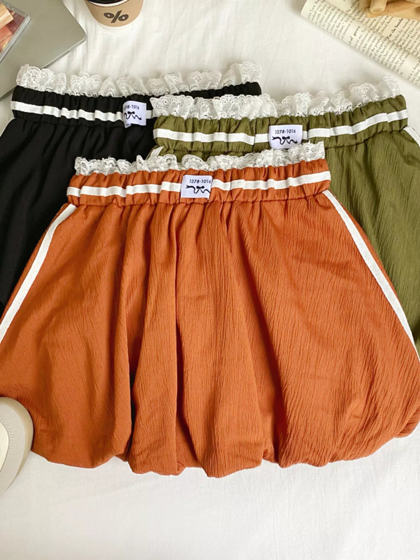 Three pairs of shorts in black, green, and orange with lace trim on a white surface.