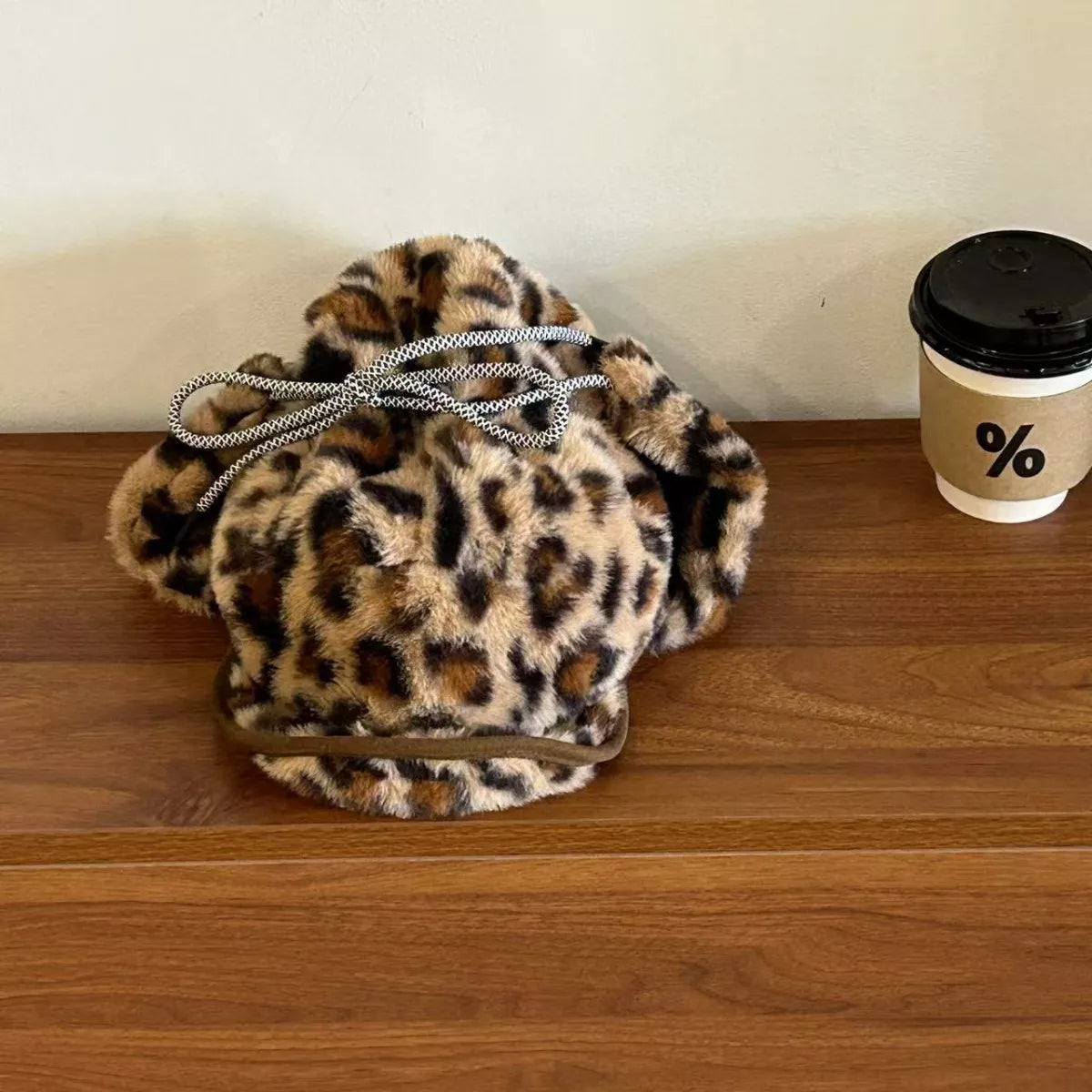 Leopard print drawstring bag on a wooden surface next to a coffee cup with a black lid.