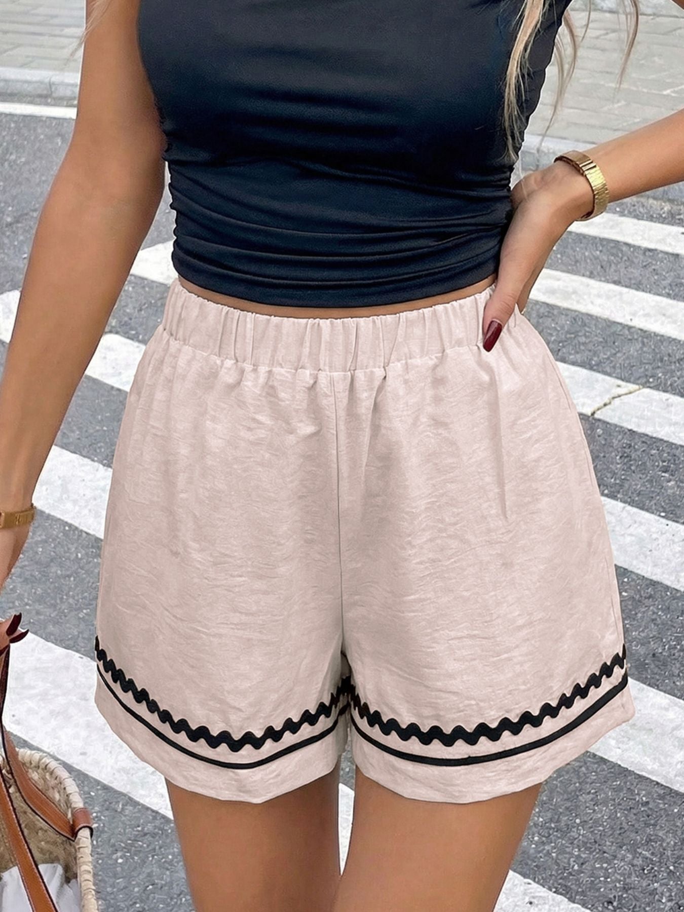 Person wearing a black sleeveless top and beige shorts with black trim on a crosswalk.