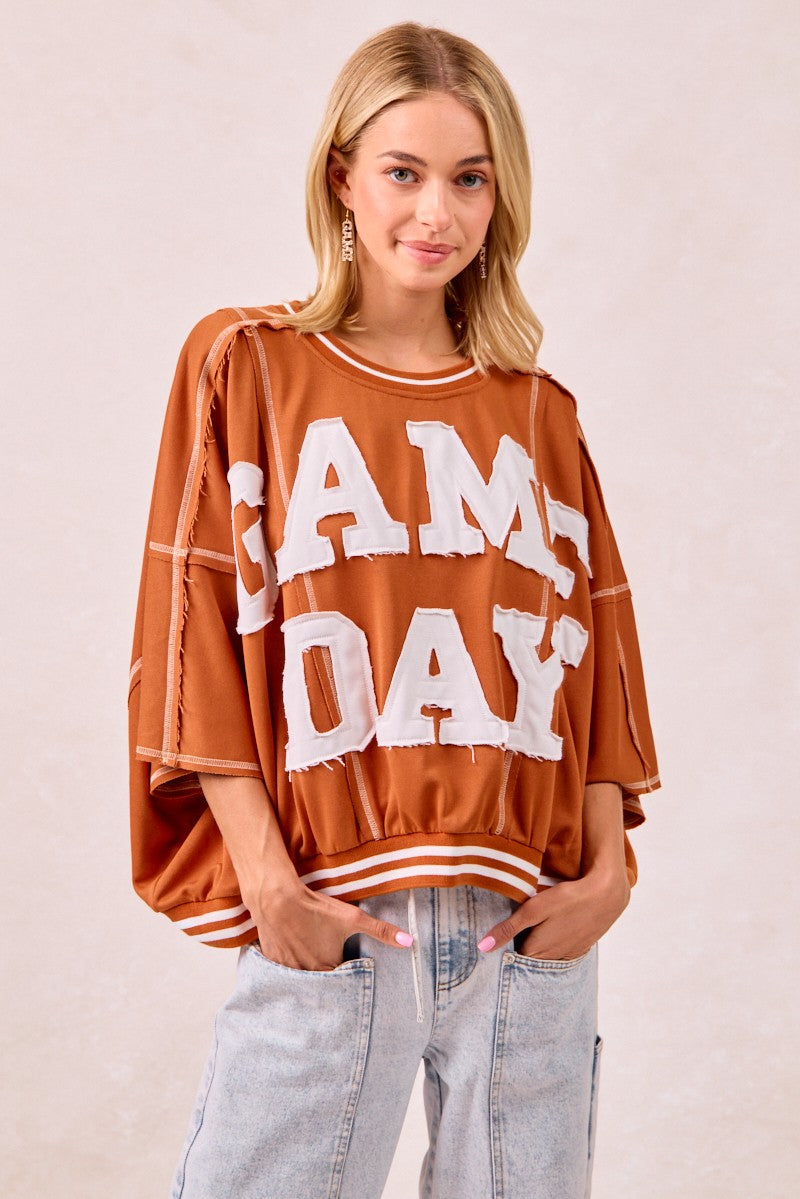 Woman wearing a brown oversized sweater with 'AM DAY' text on a plain background