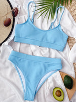 Blue bikini set on a white surface with a leaf and avocado in the background