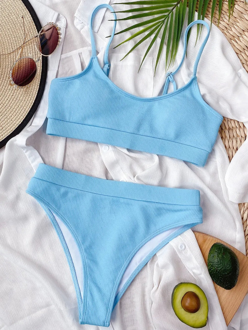 Blue bikini set on a white surface with a leaf and avocado in the background