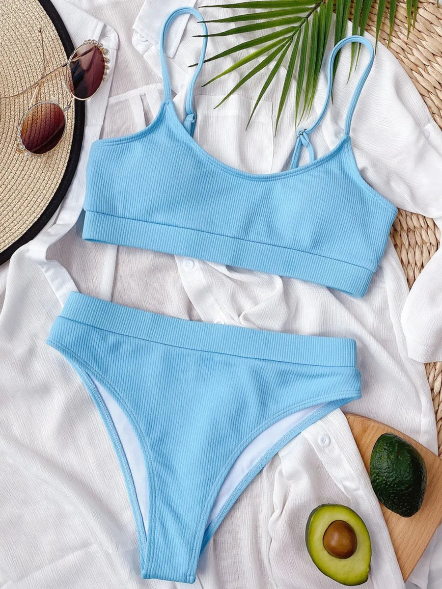 Blue bikini set on a white surface with a leaf and avocado in the background