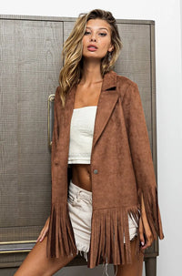 Woman wearing a brown suede jacket with fringe standing against a neutral background