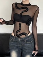 Person wearing a black sheer top with snake designs and black leather pants on a black background
