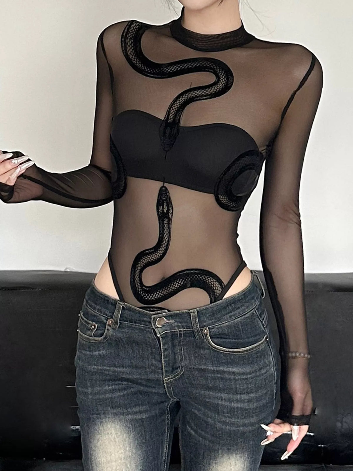 Person wearing a black sheer top with snake designs and black leather pants on a black background