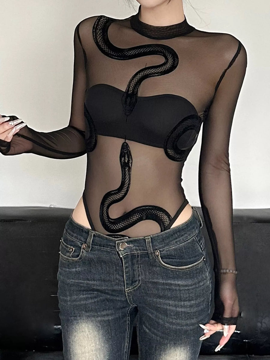 Person wearing a black sheer top with snake designs and black leather pants on a black background