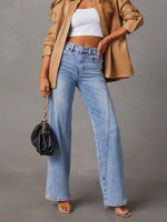 Person wearing a beige jacket, white crop top, and blue jeans holding a black handbag on a gray background