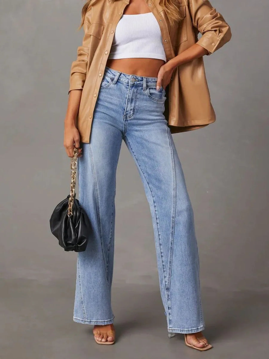 Person wearing a beige jacket, white crop top, and blue jeans holding a black handbag on a gray background