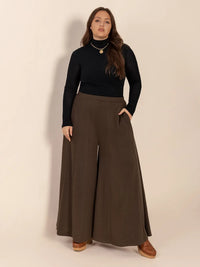 Woman wearing a black top and brown wide-leg pants on a beige background