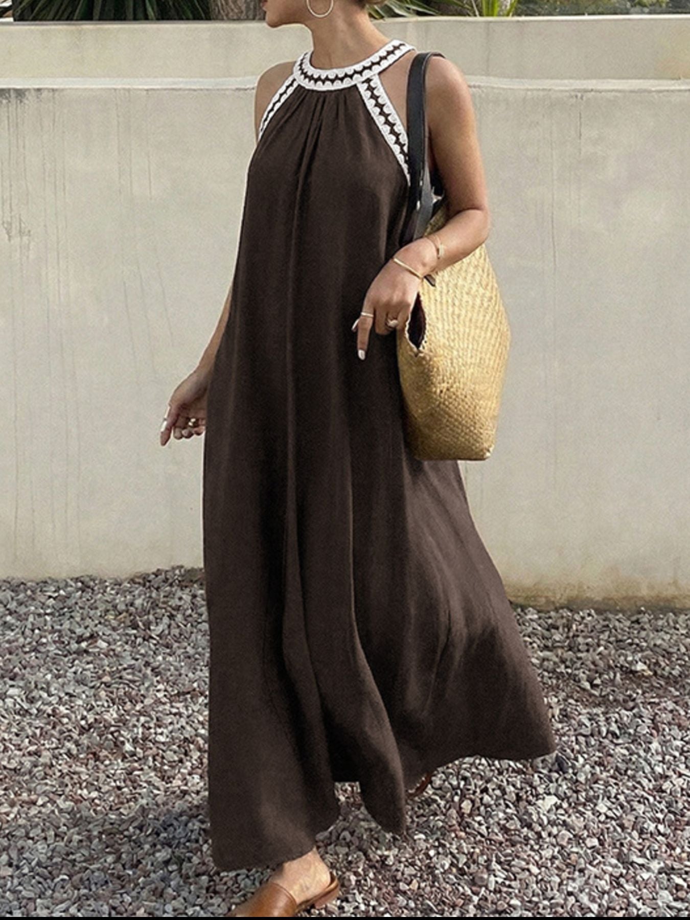 Woman wearing a brown dress with white lace details, holding a straw bag against a neutral background.