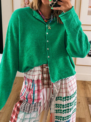 Person wearing a green cardigan over a plaid dress, taking a mirror selfie.