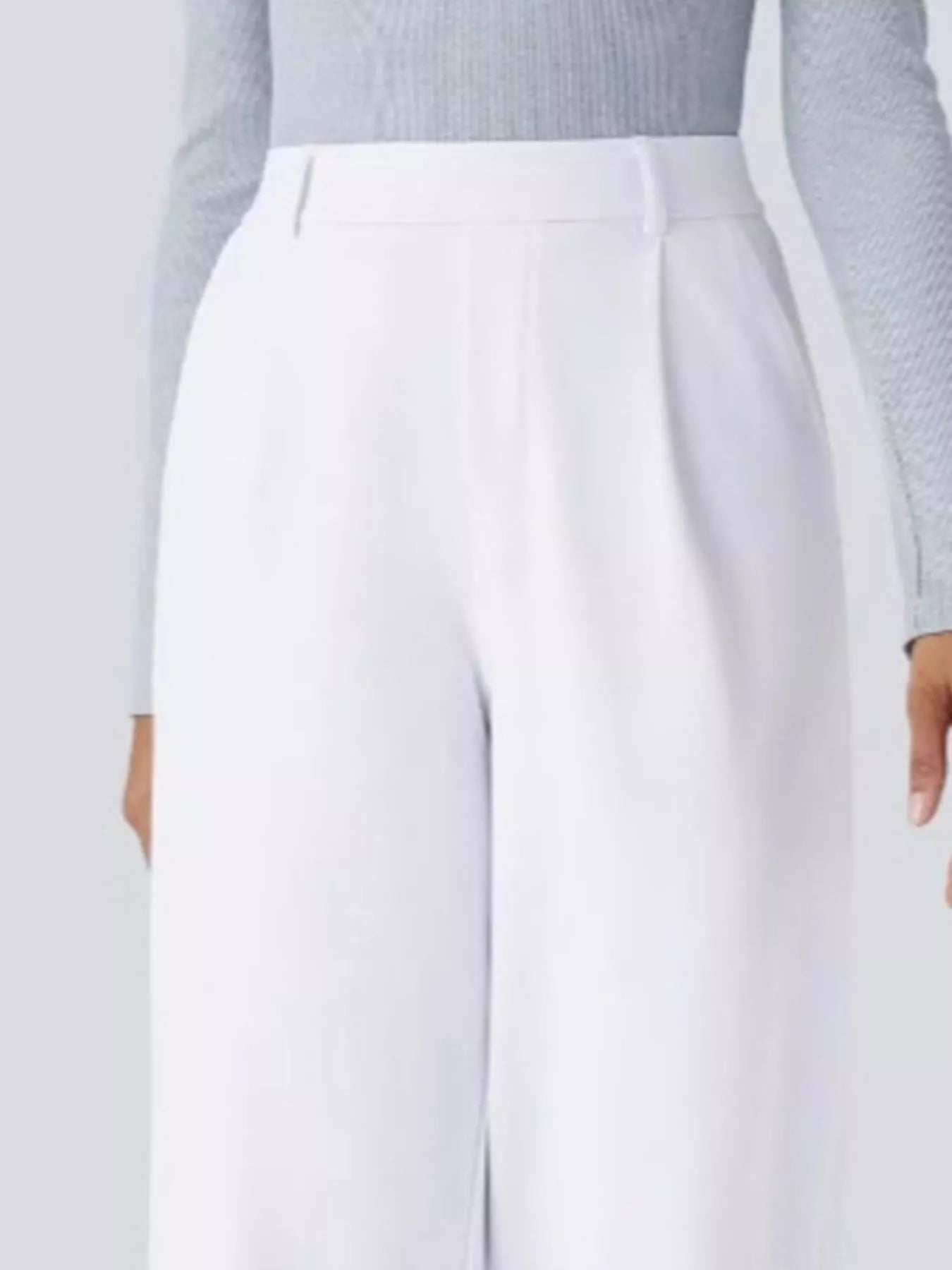 White pants worn with a light gray sweater on a plain background