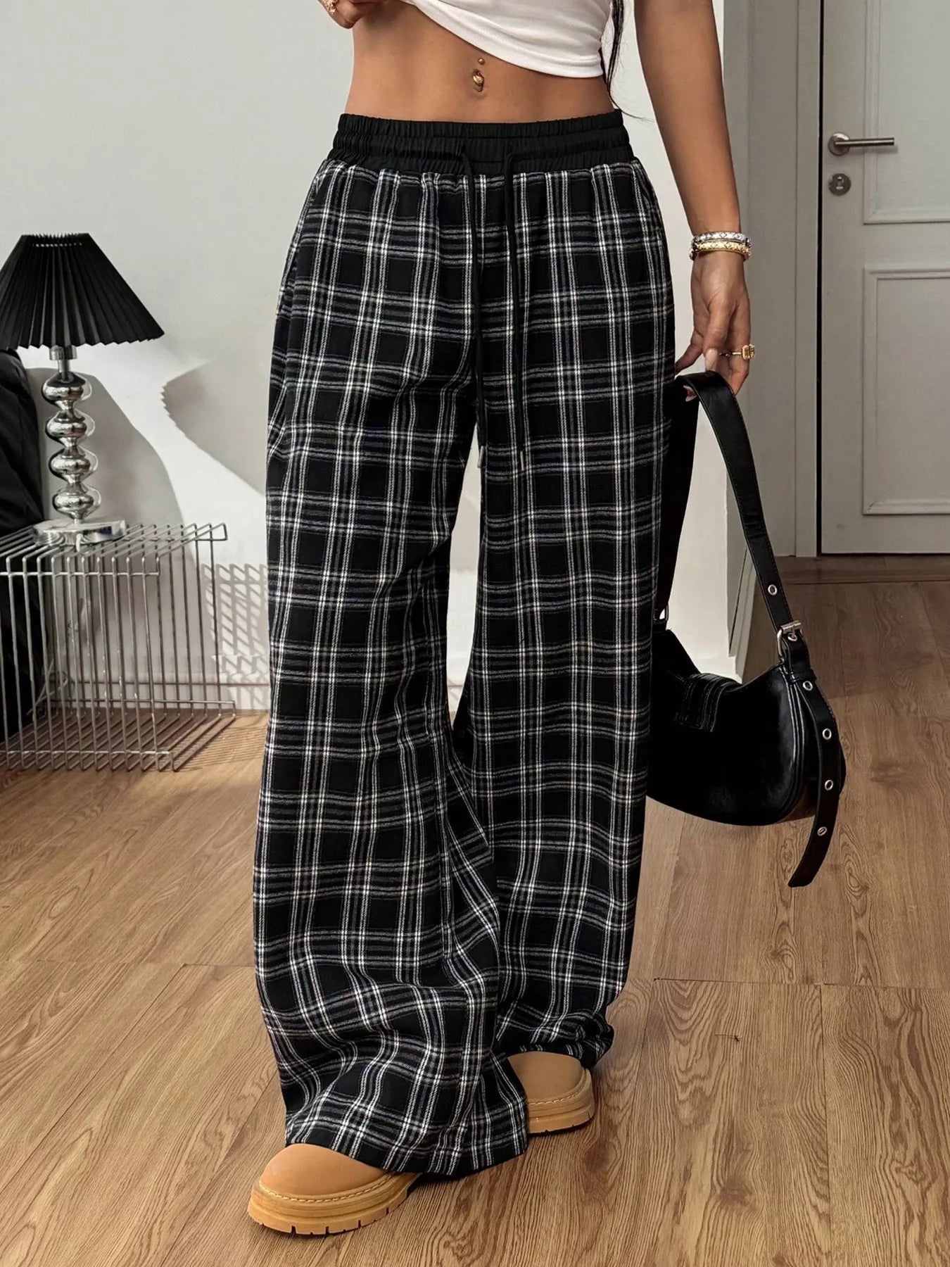 Person wearing black and white plaid pants in a room with wooden flooring.