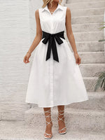 Woman wearing a white dress with a black belt standing on stone steps.