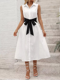 Woman wearing a white dress with a black belt standing on stone steps.