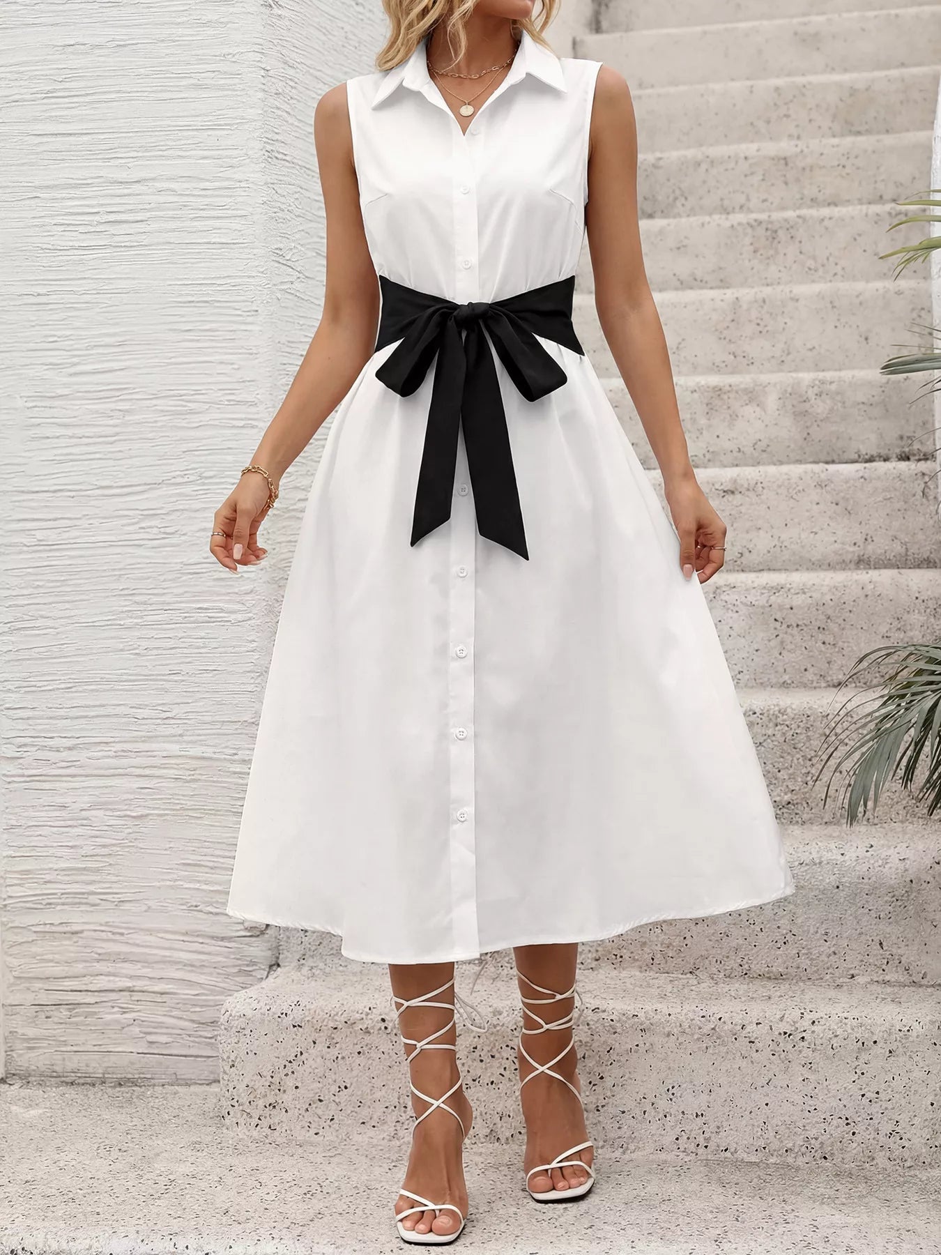 Woman wearing a white dress with a black belt standing on stone steps.