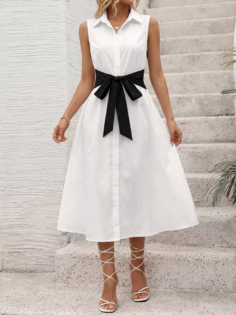 Woman wearing a white dress with a black belt standing on stone steps.
