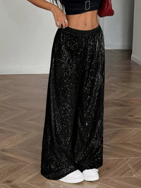 Person wearing a black sequin skirt on a wooden floor.