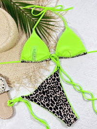 Neon green bikini top with leopard print bottom on a textured white surface.