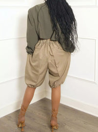 Person wearing a green top and beige baggy pants standing against a white wall.