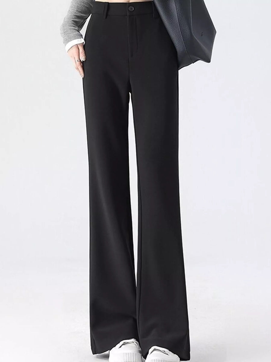 A person wearing black wide-leg trousers with a gray long-sleeve top, white sneakers, and a dark gray shoulder bag, shown from the waist down against a light gray studio background.