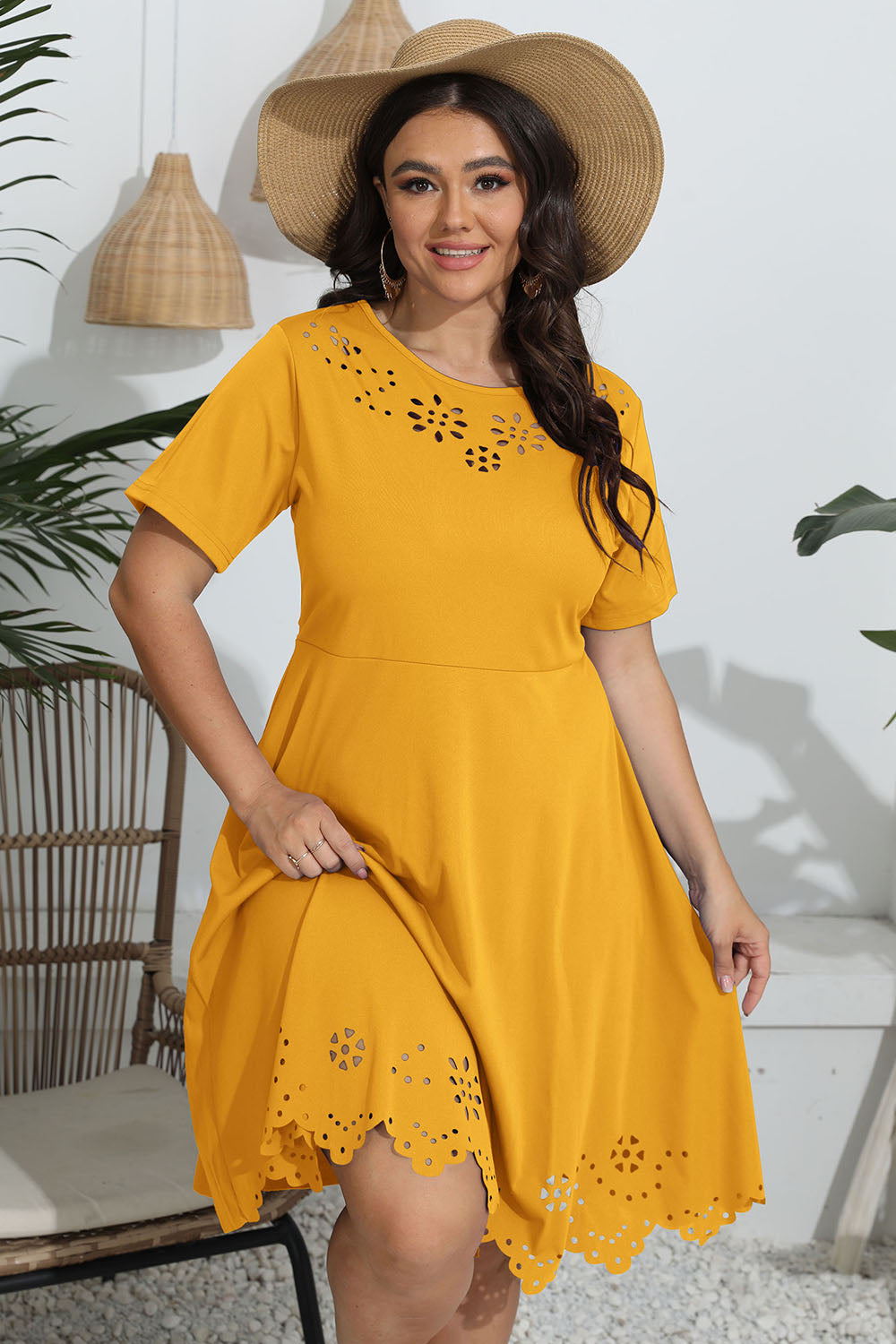 Woman wearing a yellow dress with floral cutouts and a straw hat, standing in a casual outdoor setting.