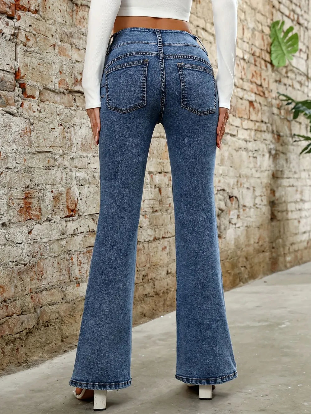Person wearing blue flared jeans standing against a brick wall.