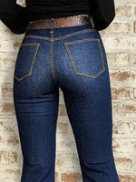 Person wearing blue jeans with a brown belt against a brick wall.